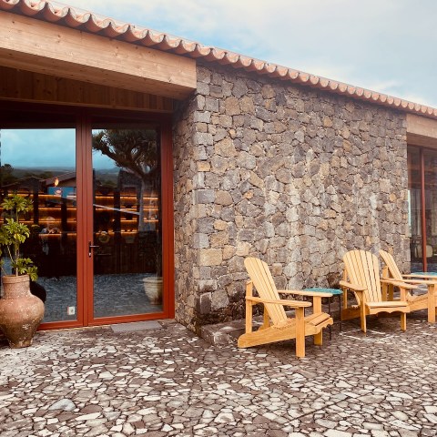 Stone building with large windows, patio with four wooden chairs and planters.