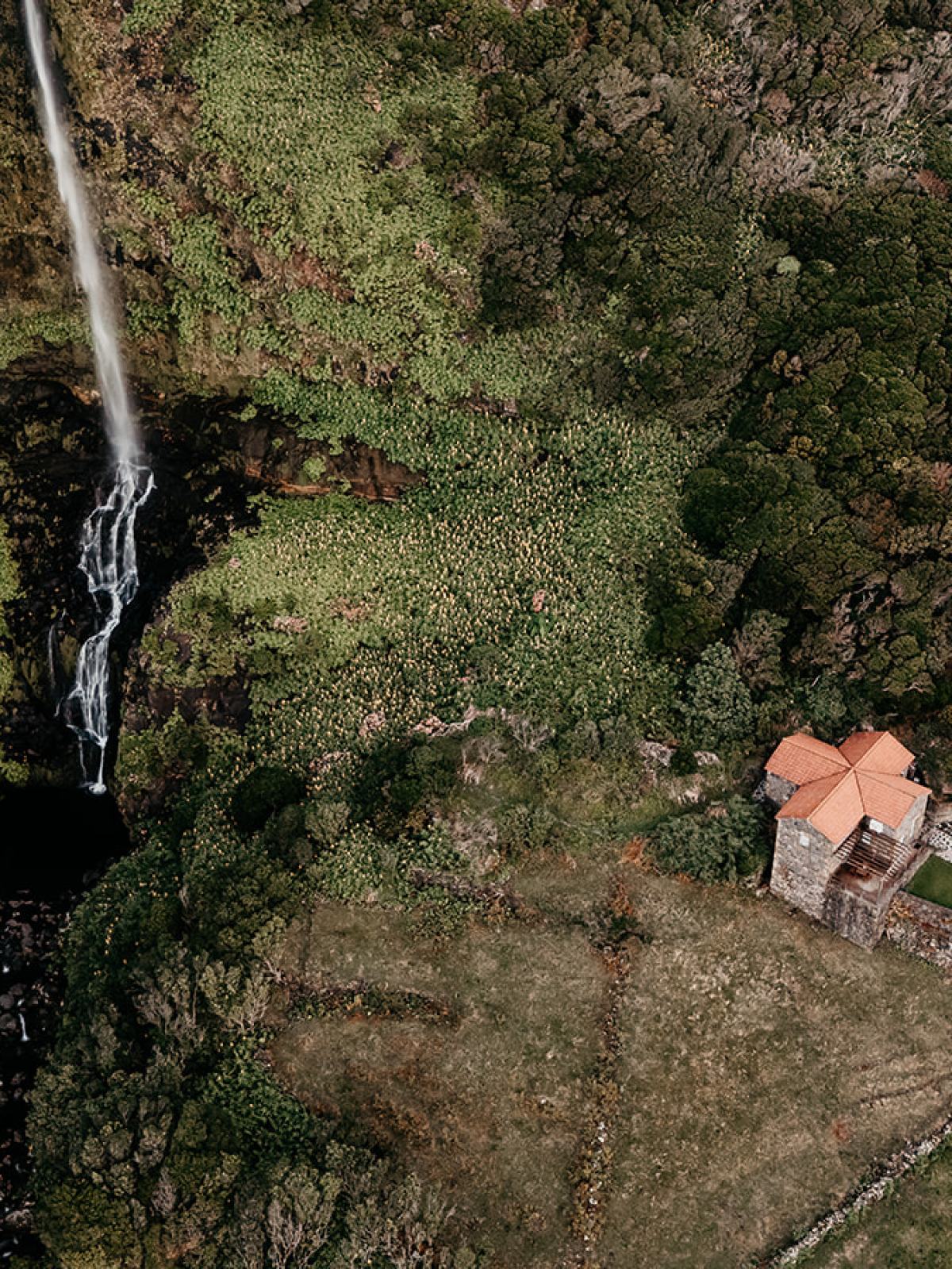 Aerial view of waterfall in lush landscape with a small house nearby.