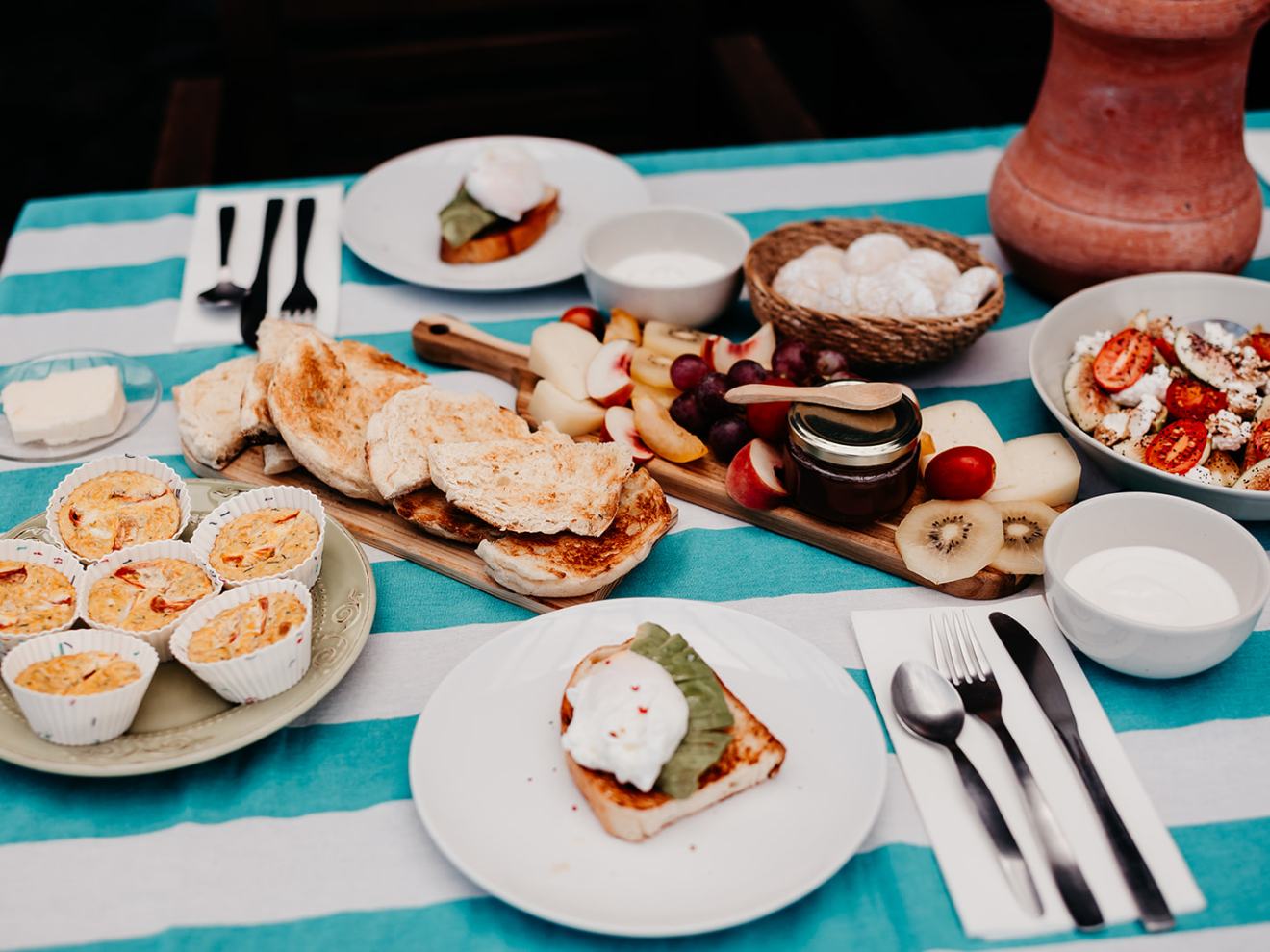 Brunch table with muffins, toast, fruit, and a salad on a striped tablecloth.