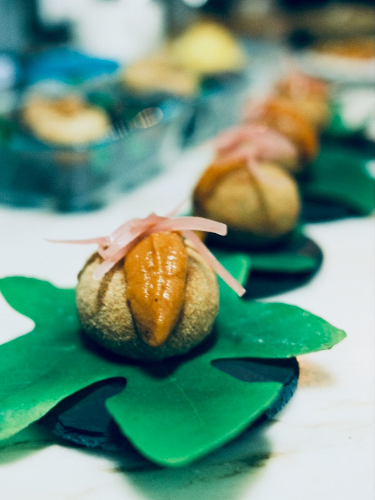 Close-up of gourmet food on green leaves, topped with orange sauce and pickled garnish.