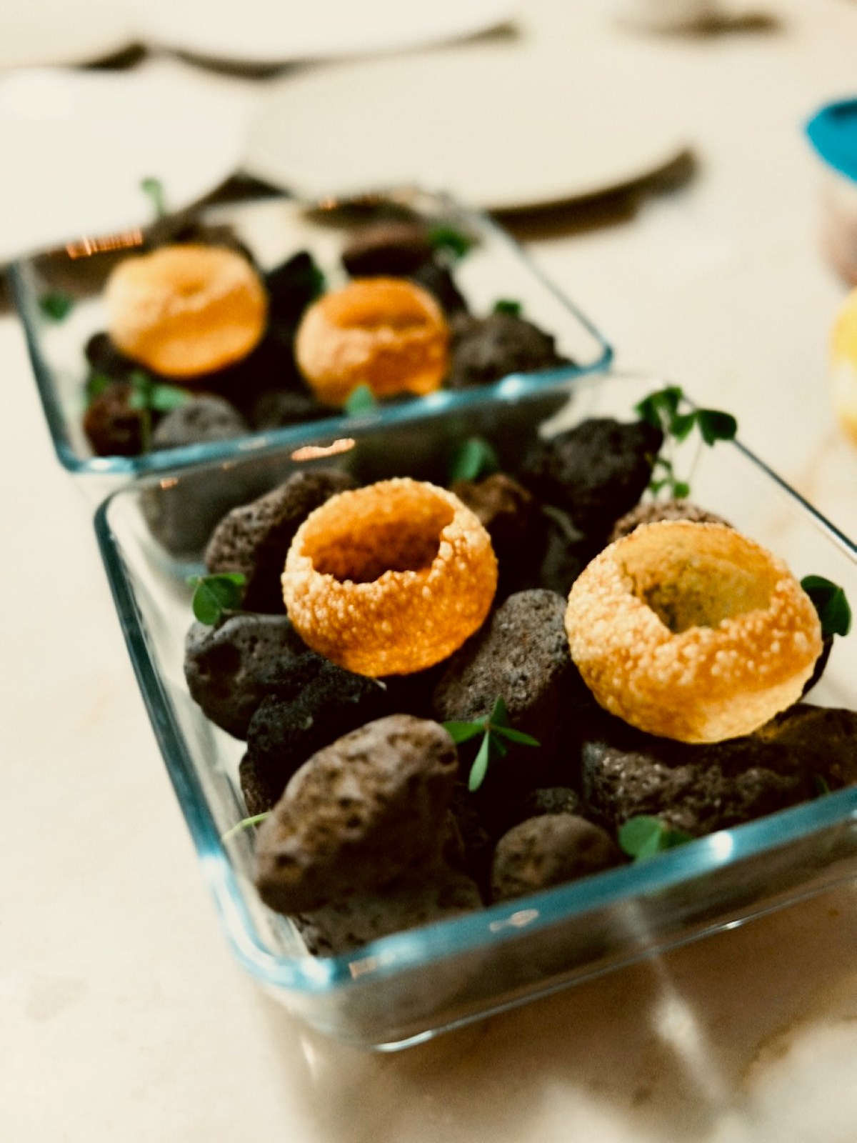Pastry shells on black stones in clear glass dishes on a table.