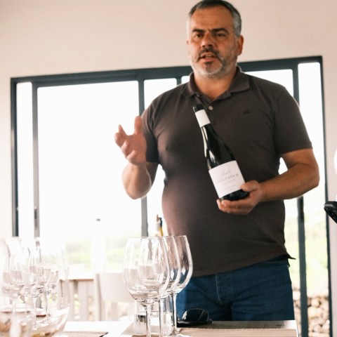 Man holding wine bottle, gesturing, with empty wine glasses on table.