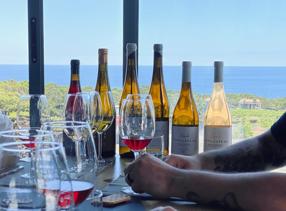 Wine bottles and glasses on a table with an ocean view in the background.