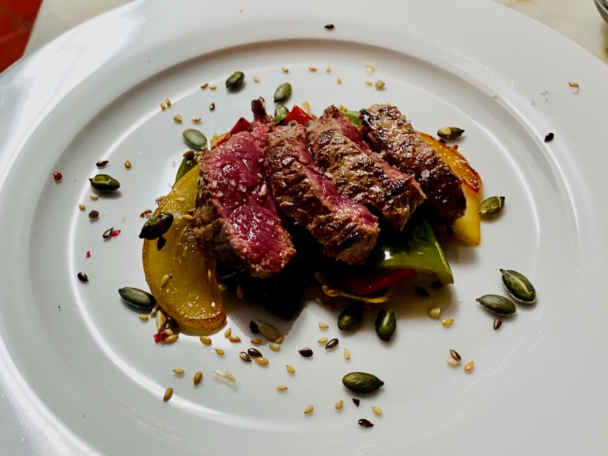 Sliced steak on vegetables with seeds on a white plate.