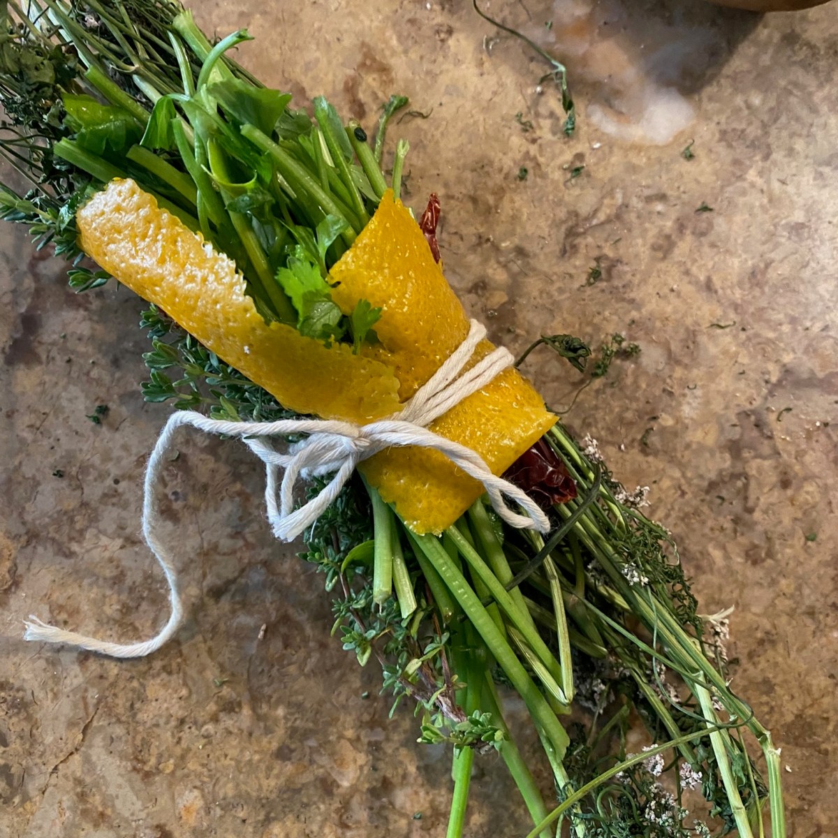 A bundle of fresh herbs tied with string and orange peel on a counter.