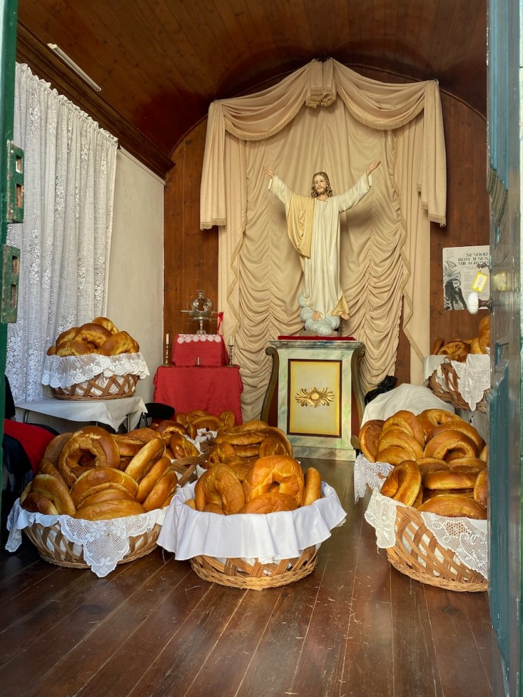 Statue of Jesus with baskets of bread in a wooden room with draped curtains.