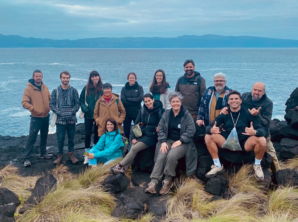 Group of people posing on rocks by the sea with distant mountains in the background.