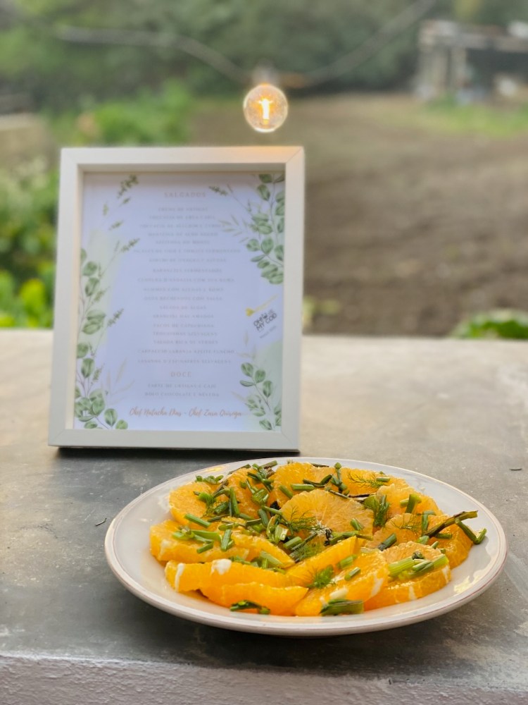Plate of sliced oranges with herbs beside a framed menu on an outdoor table.