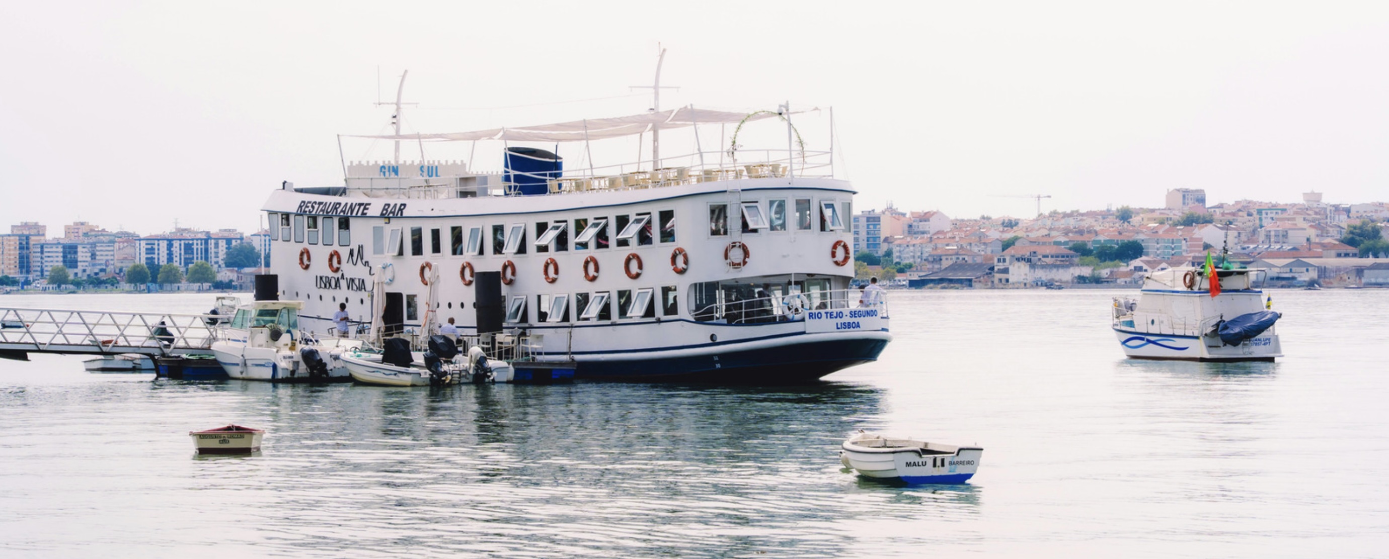 A large ferry docked near small boats on a calm river.