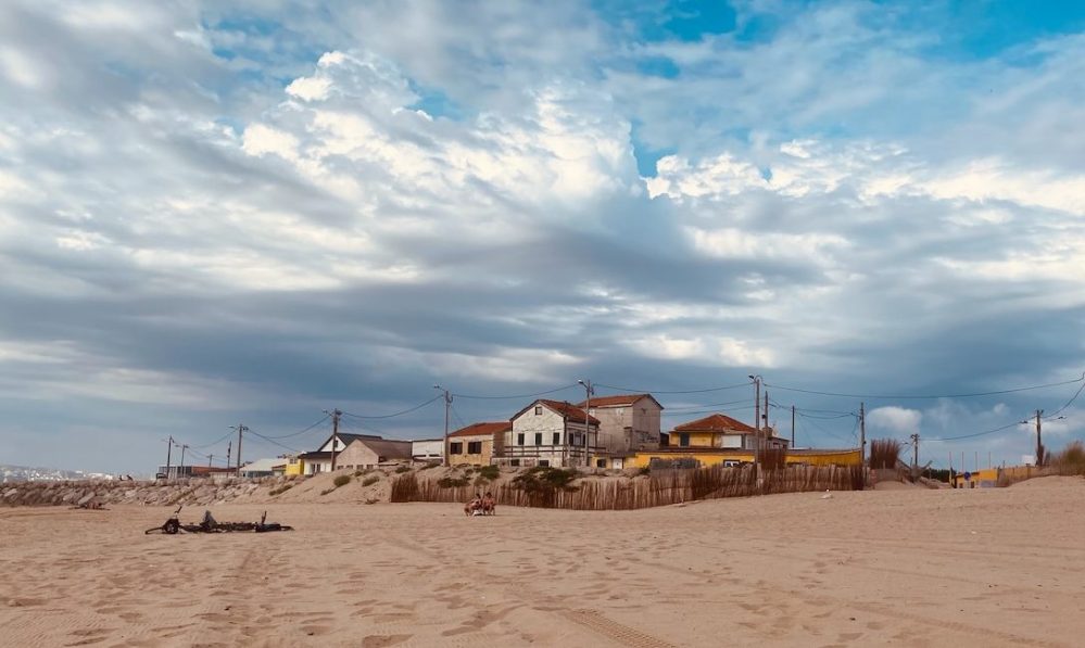 Houses on sandy beach under cloudy sky with power lines.