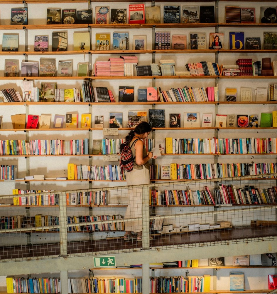 Woman browsing books on shelves in a large library with a mezzanine floor.