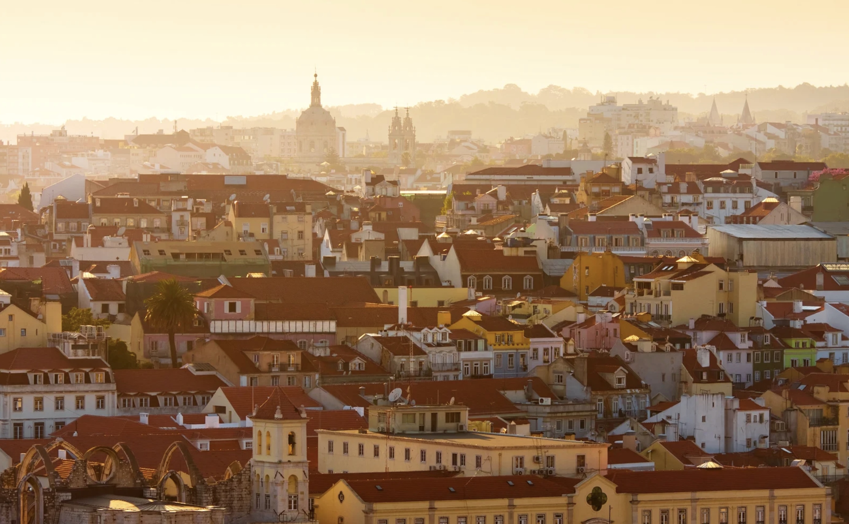 Aerial view of a city with orange rooftops and a warm sunset glow.