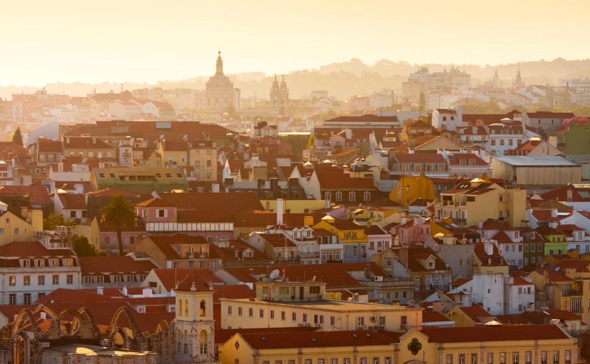 Aerial view of a city with orange rooftops and a warm sunset glow.