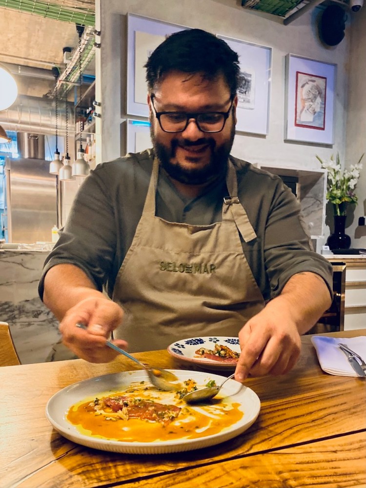 Man in apron eating soup with a smile at a restaurant table.