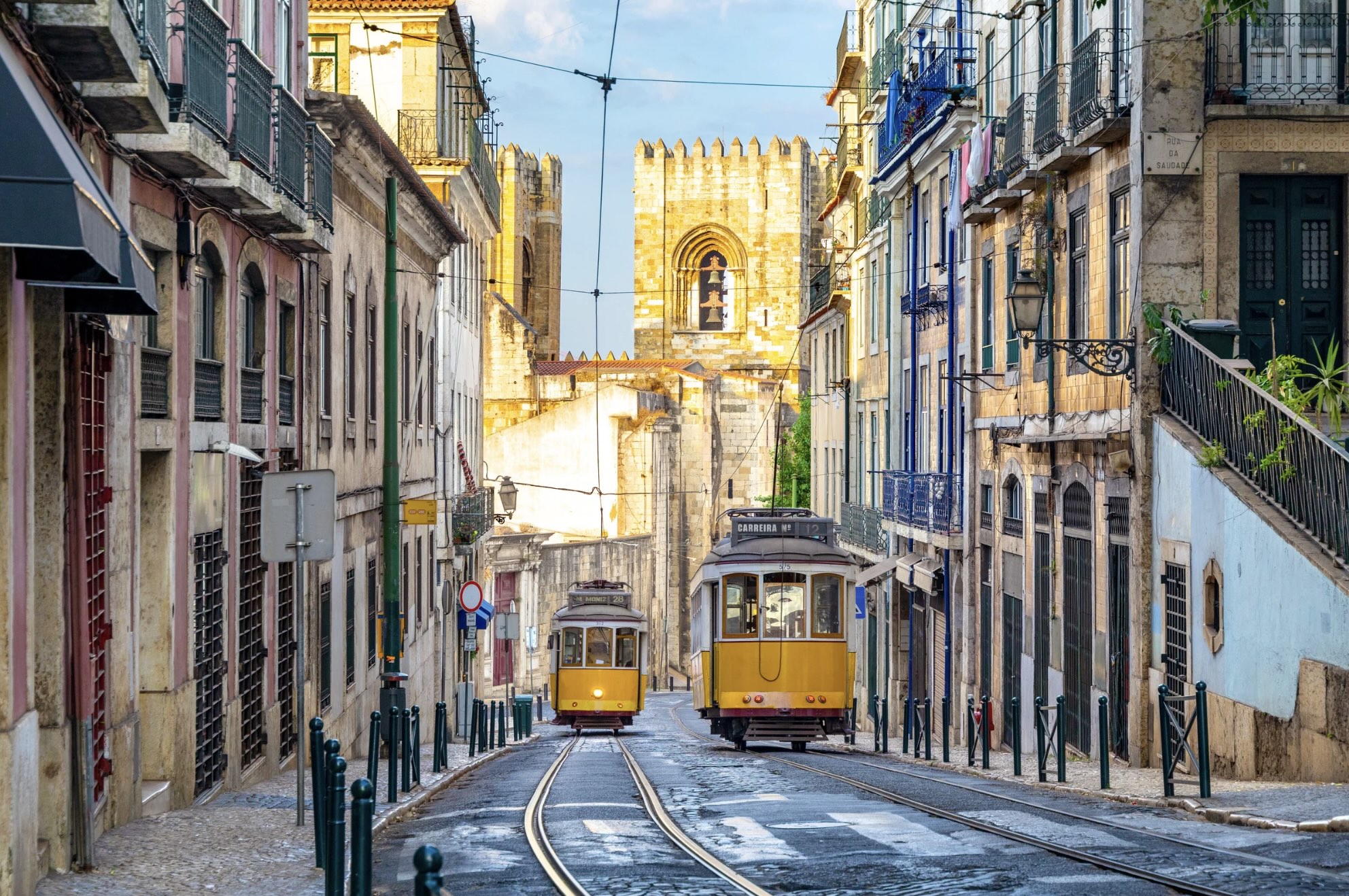 Two yellow trams on a narrow, cobbled street in a European city.
